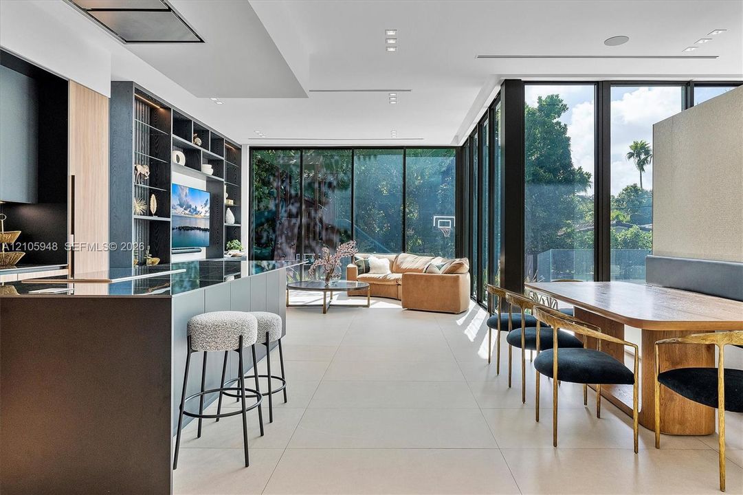 Open-concept interior featuring floor-to-ceiling black-framed windows, built-in floor-to-ceiling shelving, large-format tile flooring, and a kitchen island with stone surfacing