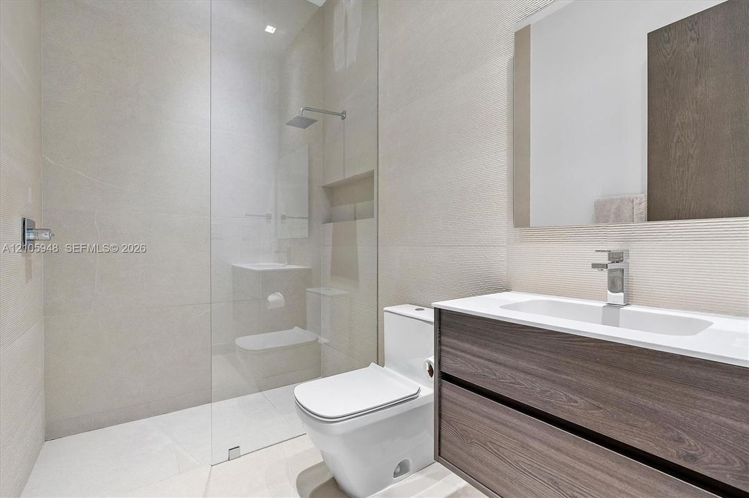 Floating vanity with wood-finish cabinetry, white countertop, integrated sink, rainfall shower head, and full-height glass shower panel