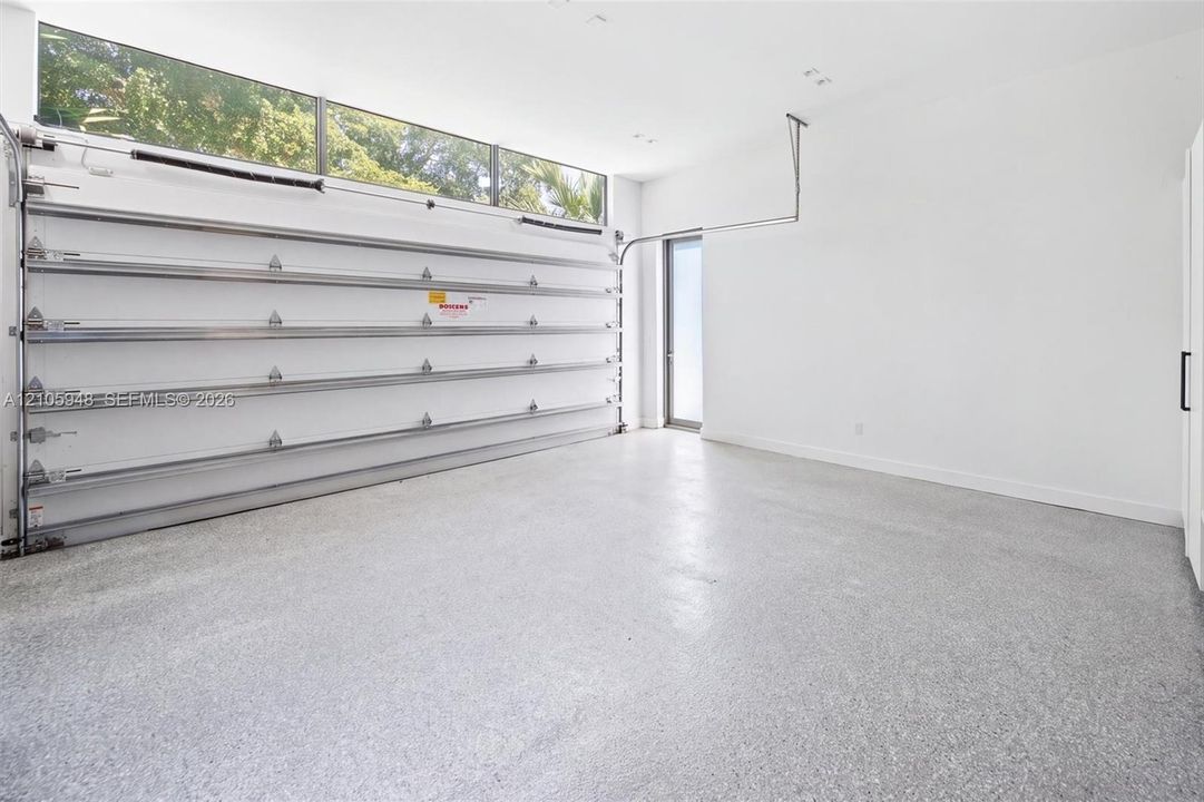 Garage space featuring speckled epoxy flooring, white paneled walls, a ceiling-mounted automatic door opener, and a row of horizontal transom windows