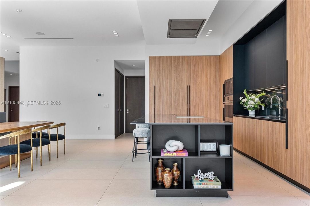 Modern kitchen featuring wood-finish cabinetry, matte black integrated shelving, a central island with storage, built-in wall appliances, and tile flooring