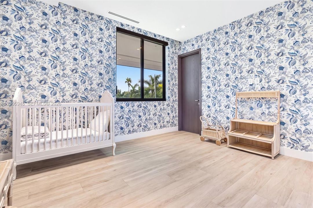 Room featuring floral patterned wallpaper, light wood-finish flooring, a black-framed window, and a dark wood-finish interior door with recessed ceiling lighting