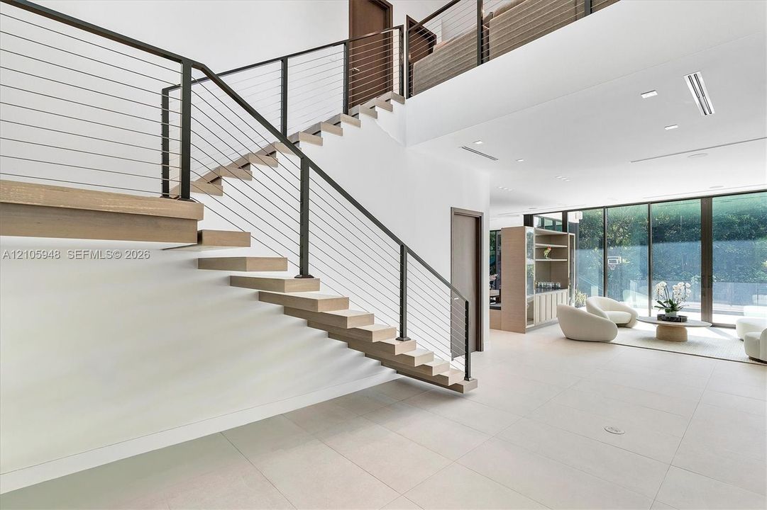 Floating staircase with wood-finish treads and horizontal cable railing, large-format tile flooring, and expansive floor-to-ceiling glass wall panels