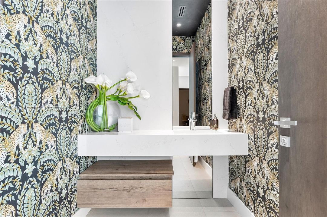Floating vanity with a stone-surface countertop, integrated basin, wood-finish cabinetry, and patterned wall covering