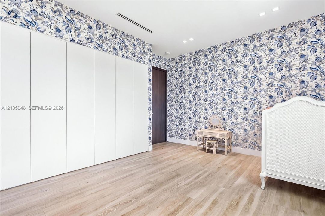 Room featuring floor-to-ceiling white cabinetry, wood-finish flooring, patterned wallpaper, recessed lighting, and a dark-finish door