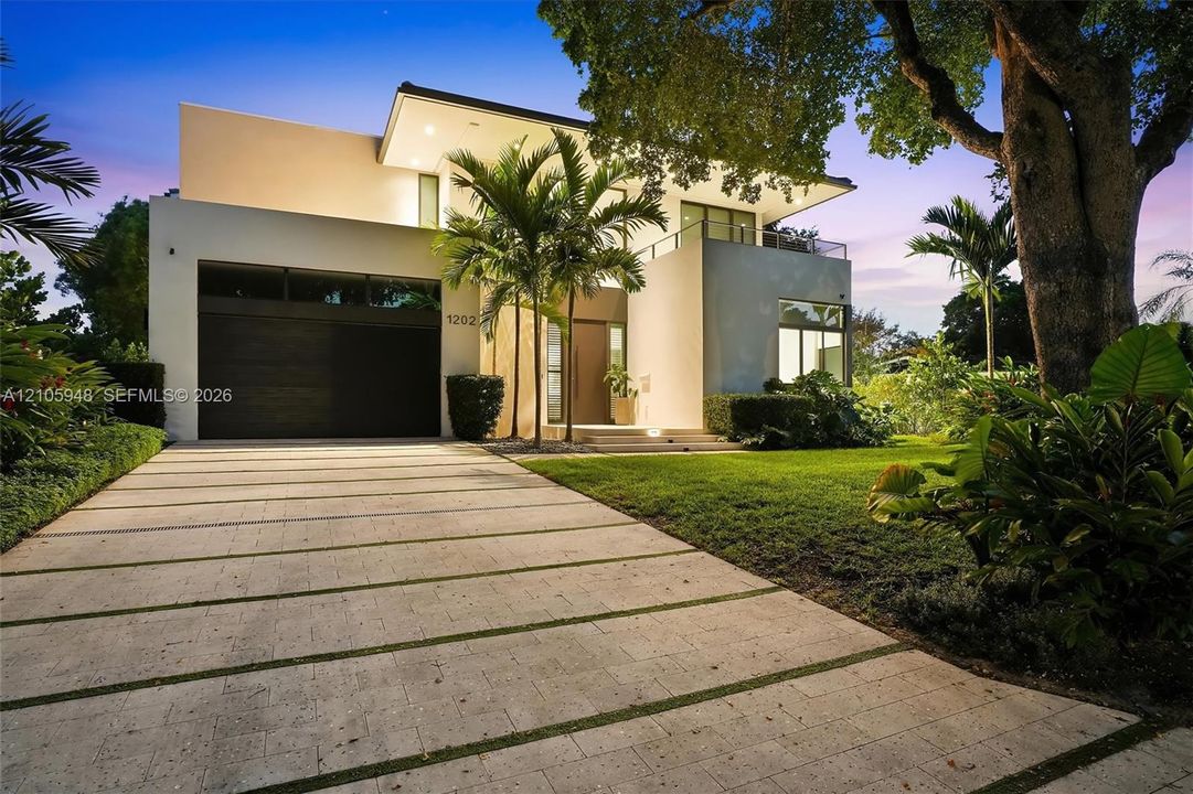 Contemporary exterior featuring smooth stucco siding, a multi-level balcony with a metal railing, a paved driveway with integrated linear landscaping, and a wood-finish garage door