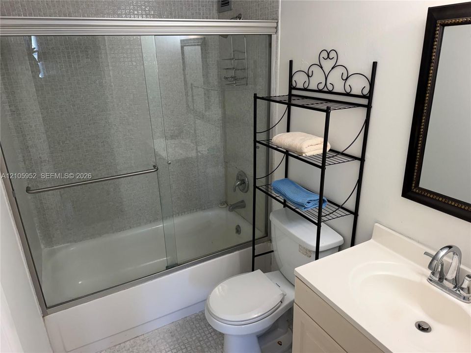 Bathroom featuring a shower-tub combination with a glass sliding enclosure, mosaic tile surround, vanity with an integrated basin, and chrome fixtures