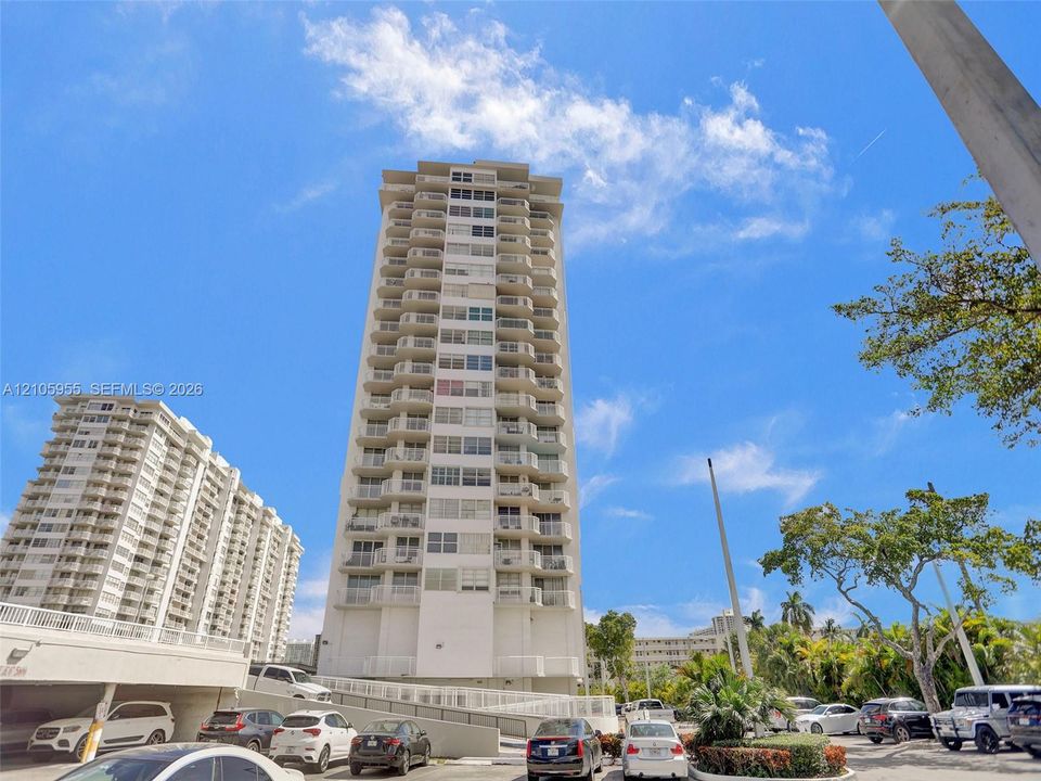 High-rise residential exterior featuring white concrete facade, stacked private balconies, and covered parking structure