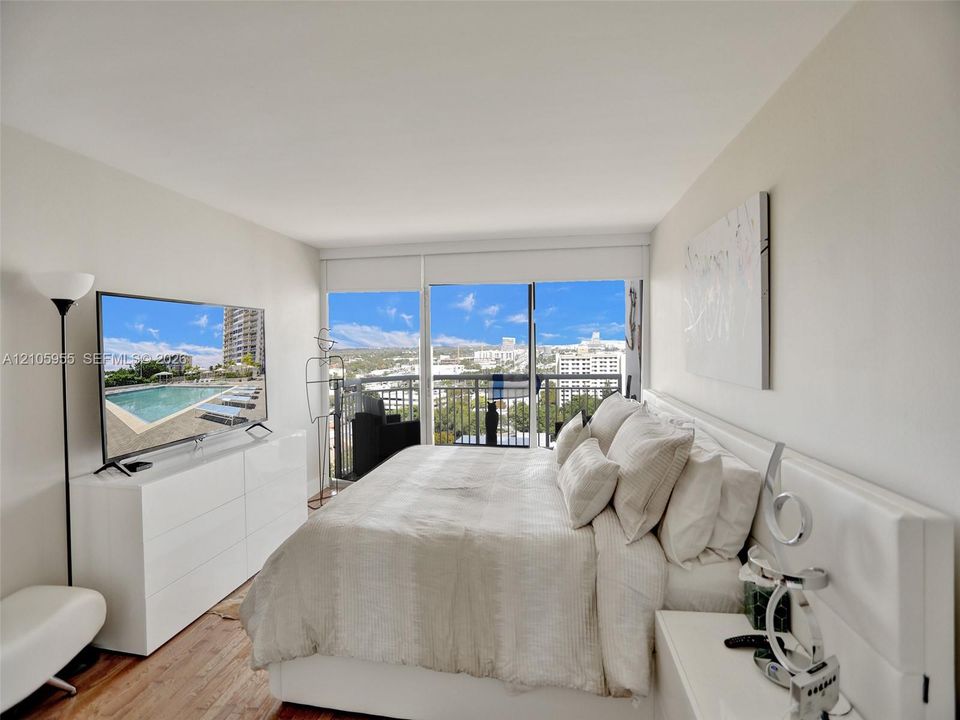 Floor-to-ceiling glass sliding doors, wood-finish flooring, metal balcony railing, and natural lighting
