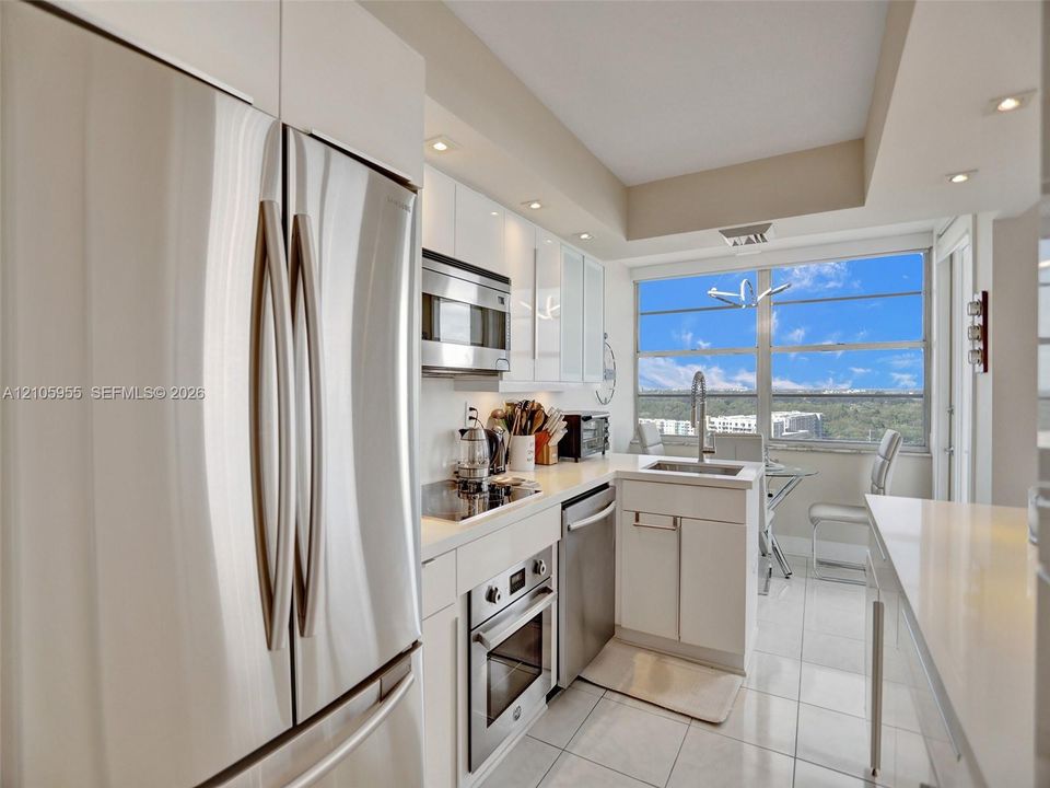Kitchen featuring high-gloss white cabinetry, stainless steel appliances, solid surface countertops, tile flooring, and large floor-to-ceiling windows