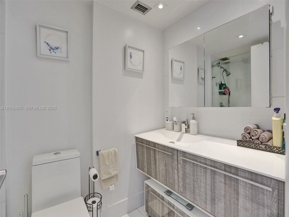 Floating vanity with wood-finish cabinetry, integrated dual-basin sink, oversized frameless mirror, and glass-enclosed shower
