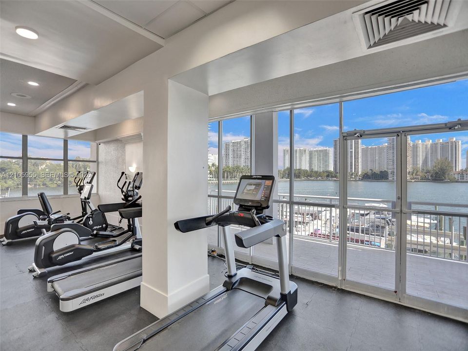 Fitness center featuring expansive floor-to-ceiling windows, dual glass doors, recessed lighting, and rubber flooring