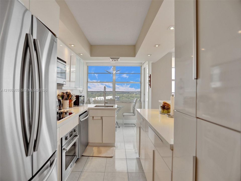 Kitchen featuring high-gloss cabinetry, stainless steel appliances, solid-surface countertops, tile flooring, and large window