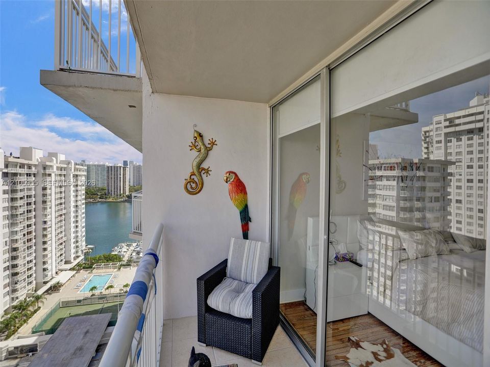 Covered balcony featuring white tiled flooring and a metal railing, floor-to-ceiling sliding glass doors, and panoramic urban and water surroundings