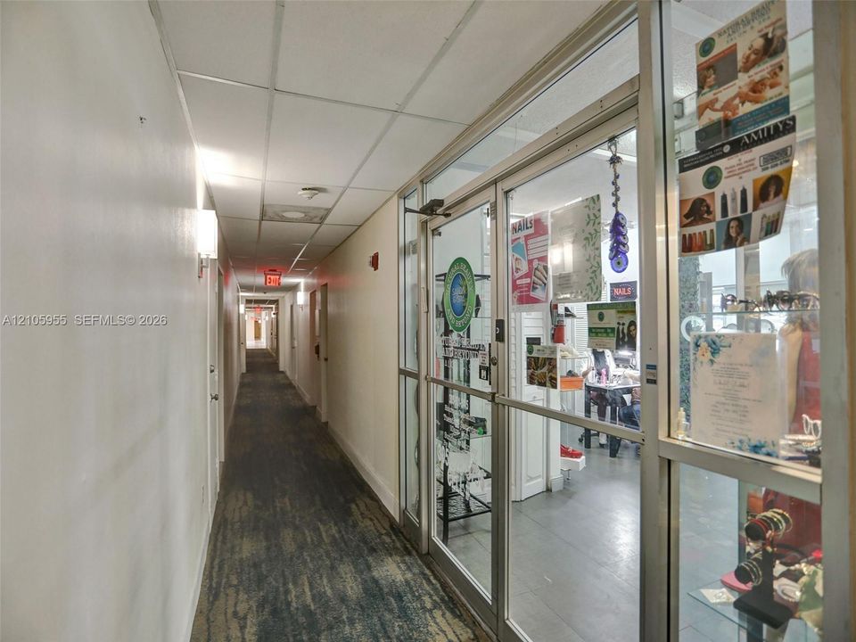 Commercial hallway featuring drop-ceiling tiles, recessed lighting, and glass-paneled entry doors with aluminum framing