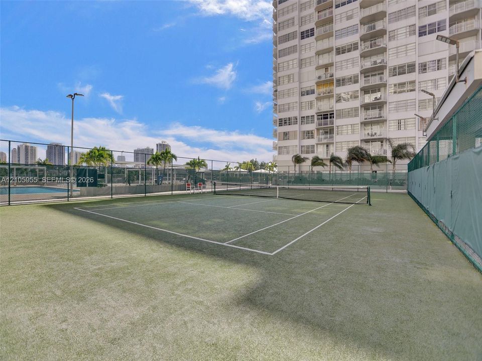 Tennis court with synthetic turf surface, enclosed by perimeter chain-link fencing