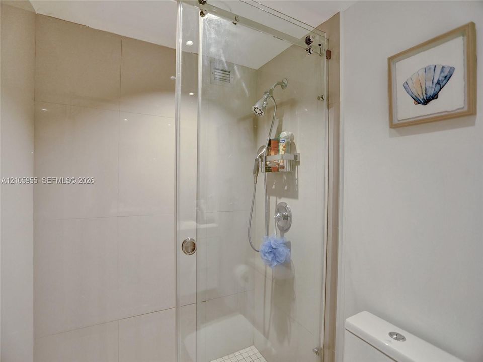 Walk-in shower with floor-to-ceiling tile, frameless glass sliding enclosure, polished chrome rainfall showerhead, and handheld sprayer