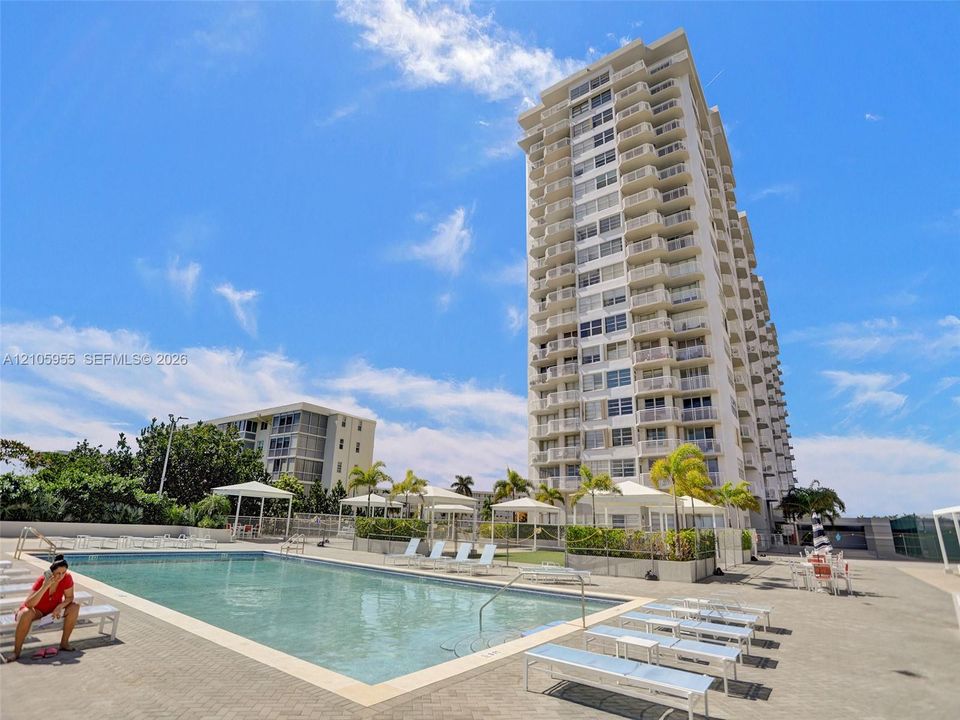 High-rise residential building featuring multiple private balconies, a ground-level swimming pool, and dedicated cabana structures