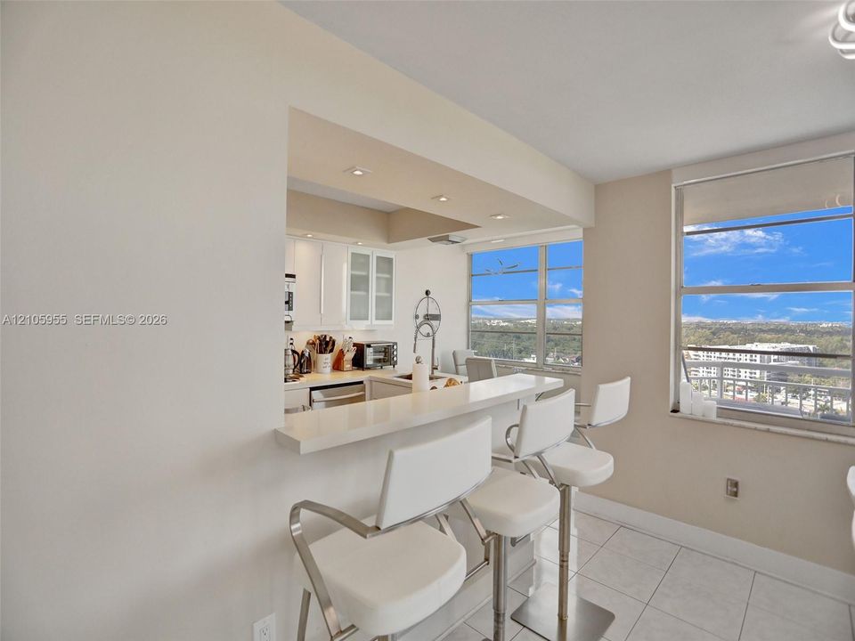 Kitchen featuring a white quartz breakfast bar, white cabinetry with glass-front accents, recessed lighting, and large windows with exterior scenery