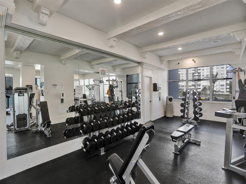 Fitness area featuring rubberized flooring, expansive wall-to-wall mirrors, exposed ceiling beams with corbel detailing, and oversized windows