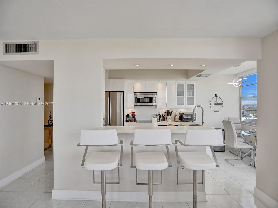 Kitchen featuring white cabinetry, stainless steel appliances, recessed lighting, and a breakfast bar with a solid surface countertop
