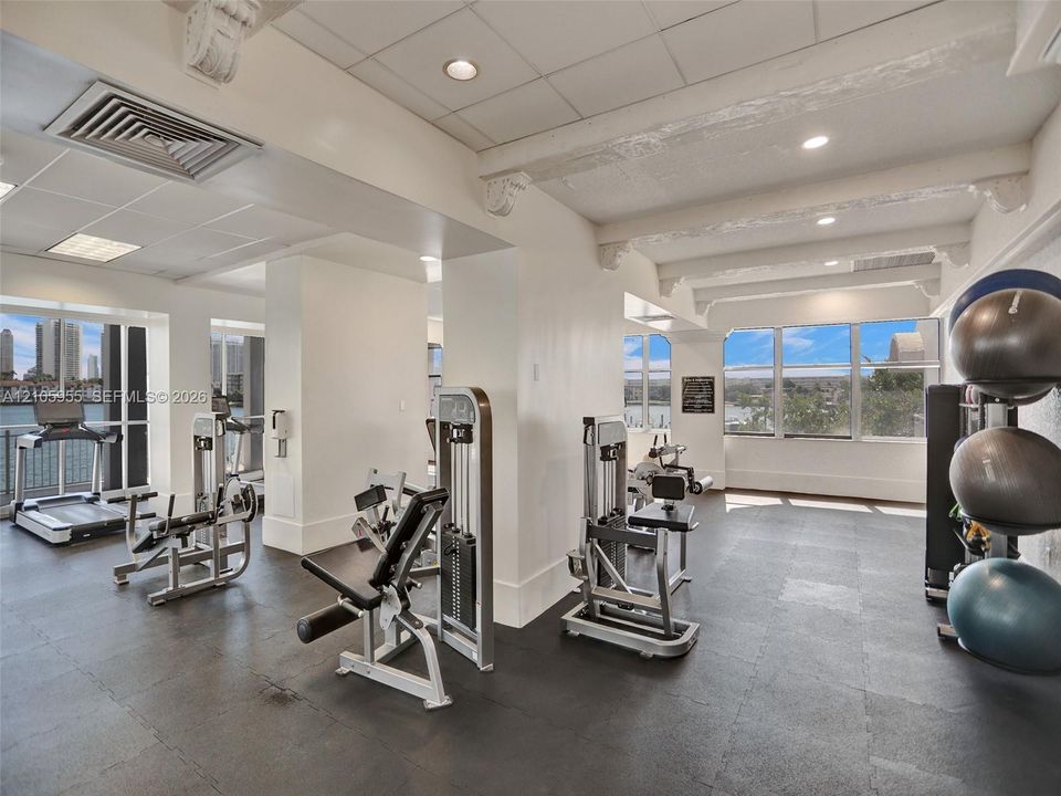 Fitness center featuring high ceilings with exposed decorative corbels, resilient flooring, extensive window walls, and recessed lighting