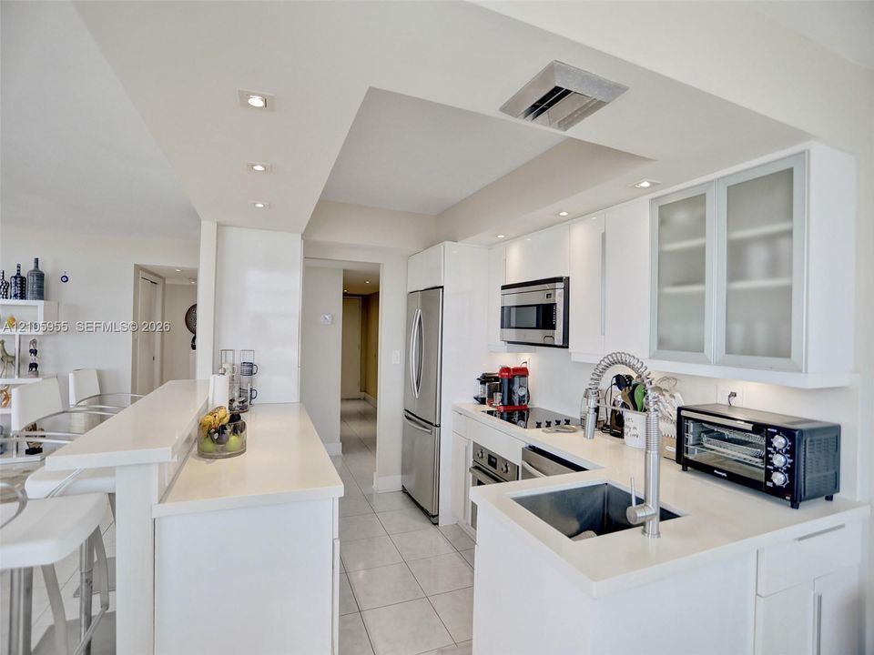 Kitchen featuring white cabinetry, frosted glass cabinet doors, quartz countertops, stainless steel appliances, and tile flooring