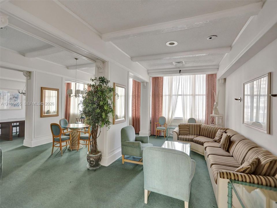 Expansive living area featuring beamed ceilings, floor-to-ceiling windows, wall-mounted light fixtures, and architectural columns