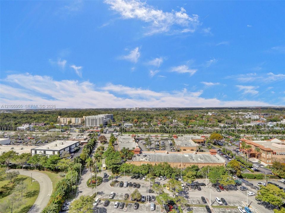 Aerial perspective of the surrounding commercial district featuring expansive paved parking areas, dense perimeter landscaping, and established tree canopy