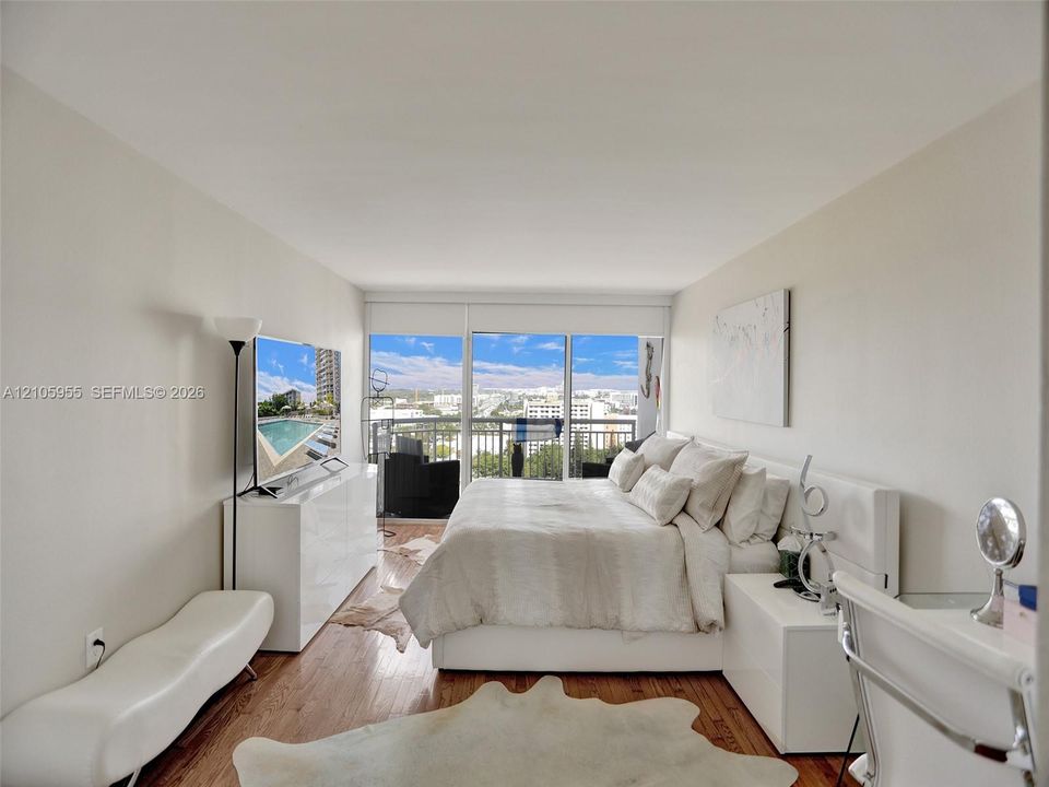 Floor-to-ceiling windows, wood-finish flooring, and an attached balcony featuring a metal railing