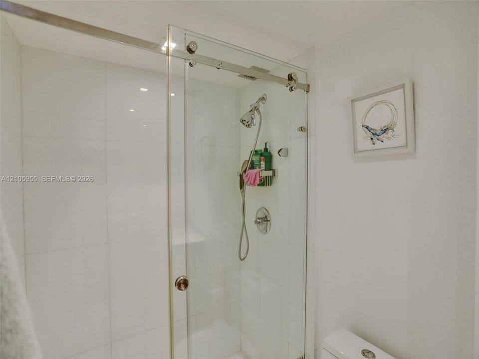 Shower enclosure featuring a frameless glass sliding door, polished metal hardware, large-format white wall tile, and an adjustable handheld shower fixture
