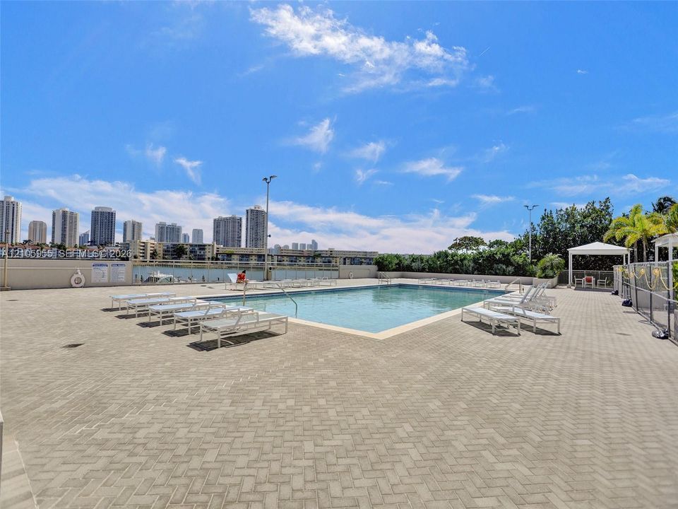 Swimming pool with a paved deck, perimeter fencing, and an overhead pavilion structure