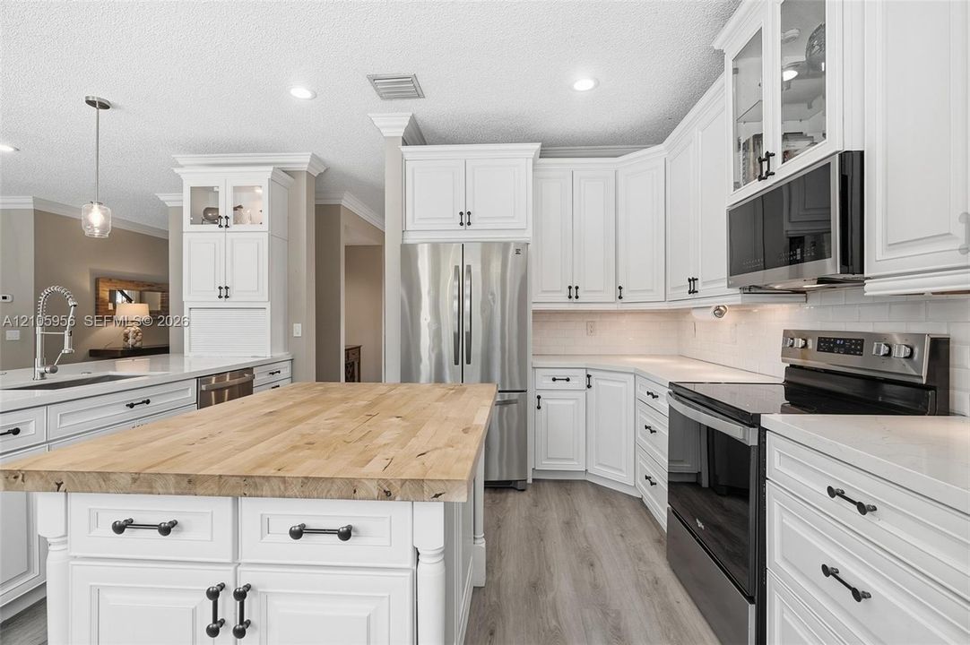 Kitchen featuring white shaker-style cabinetry, wood-top center island, stainless steel appliances, light-toned countertop surfaces, and wood-finish flooring