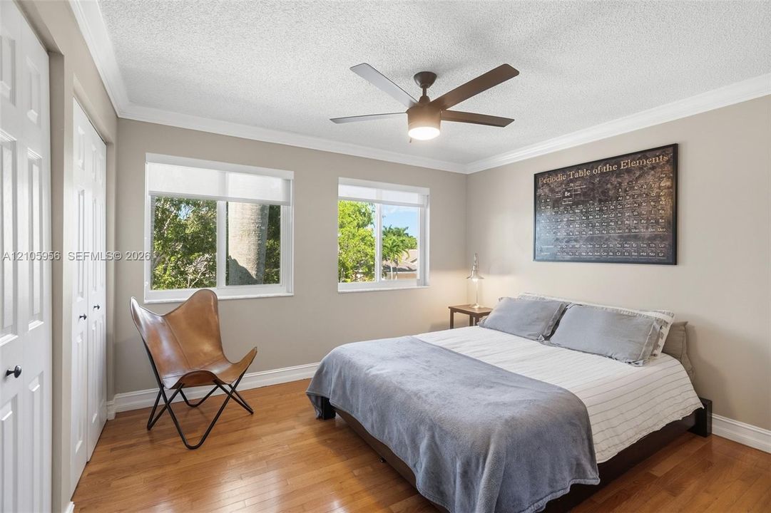 Room featuring wood-finish flooring, dual windows with roller shades, ceiling fan with integrated lighting, and multi-panel closet doors