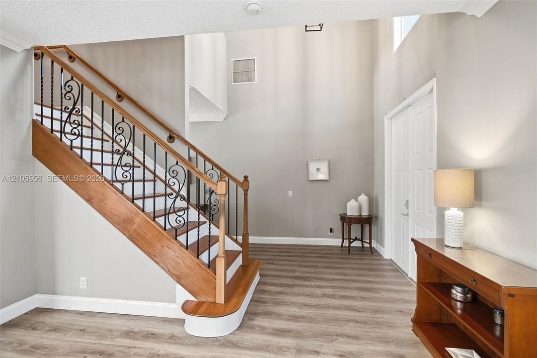 Two-story foyer featuring high ceilings, wood-finish flooring, and a staircase with decorative wrought-iron balusters and a natural wood handrail