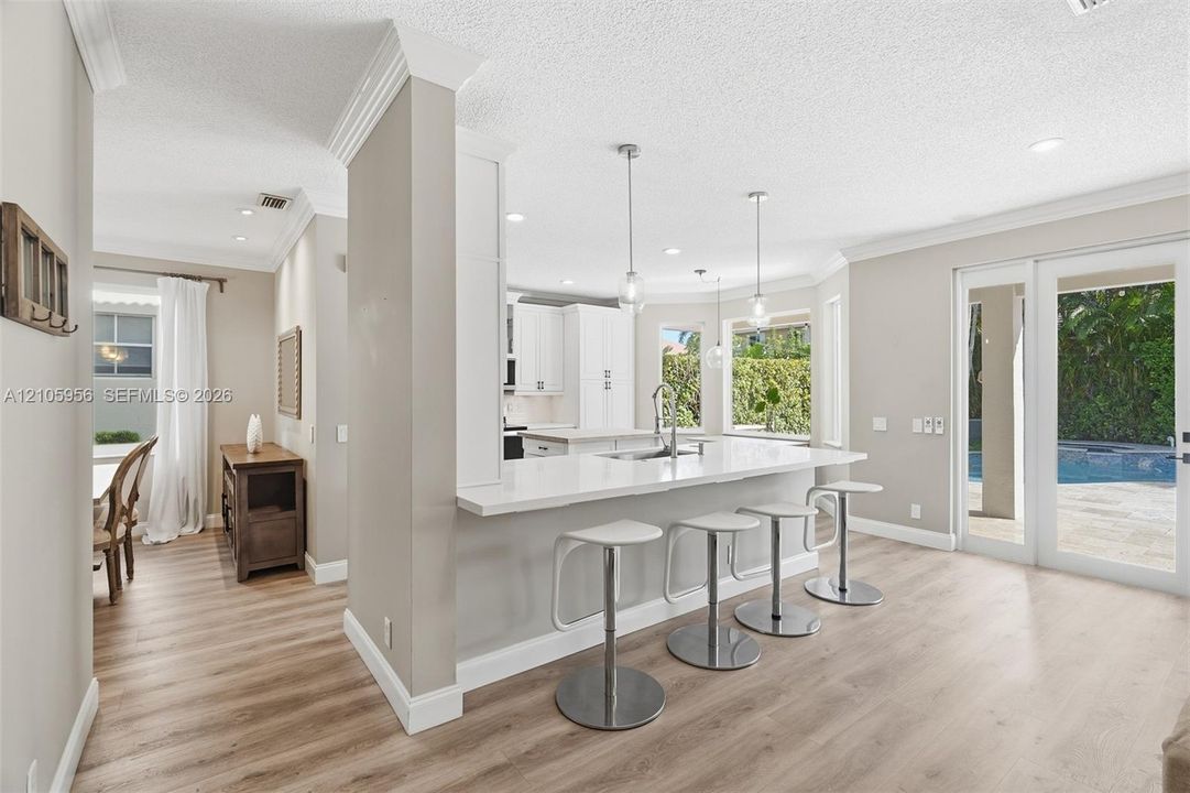Kitchen featuring white shaker-style cabinetry, quartz countertops with a breakfast bar, stainless steel undermount sink, wood-finish flooring, and recessed lighting