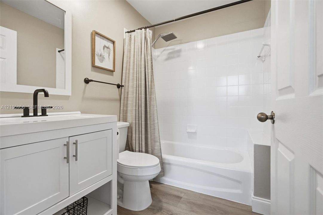 Bathroom featuring a white vanity cabinet with a rectangular undermount sink, matte black faucet hardware, wood-finish flooring, and a tiled shower-tub combination