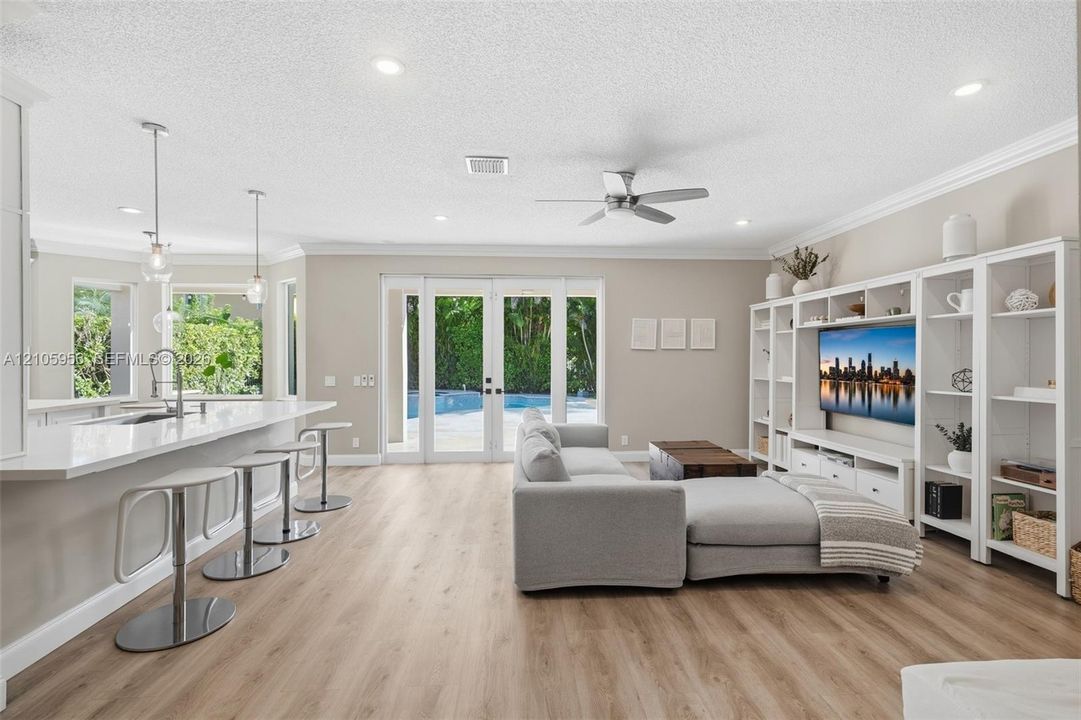 Open-concept living space featuring wood-finish flooring, recessed lighting, a built-in entertainment center, a kitchen island with stone-surface countertops, and glass-paneled double doors