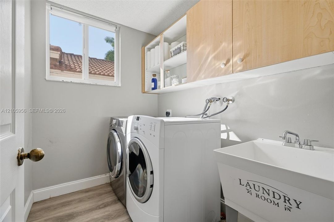 Laundry area featuring light wood-finish cabinetry, built-in shelving, a utility sink with a chrome faucet, and wood-finish flooring