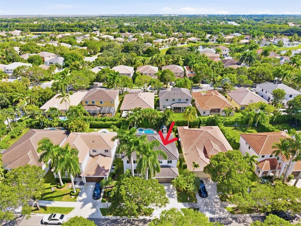 Aerial perspective featuring a two-story residence with a concrete tile roof, integrated swimming pool, attached multi-car garage, and mature palm trees