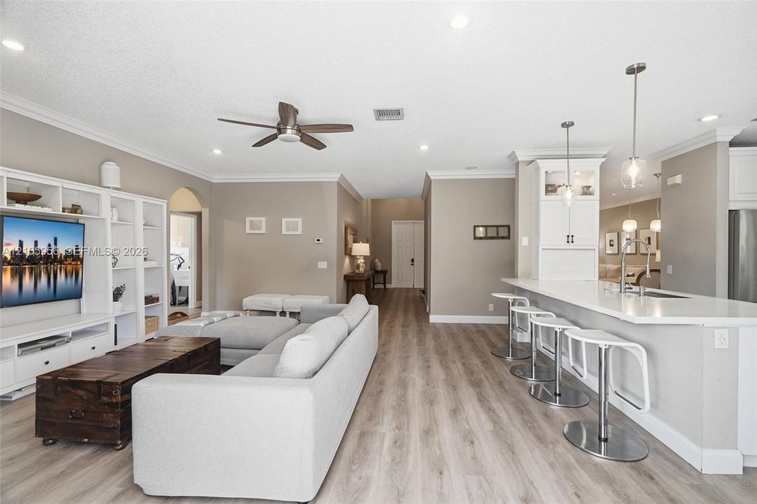 Open-concept interior featuring wood-finish flooring, built-in cabinetry, recessed lighting, and a breakfast bar with stone-surface countertops and pendant lighting