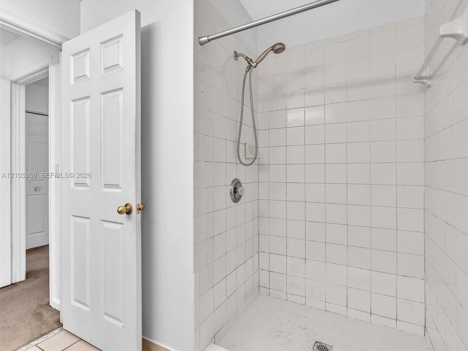 Walk-in shower featuring white tiled walls, a handheld showerhead, a metal curtain rod, and a towel bar