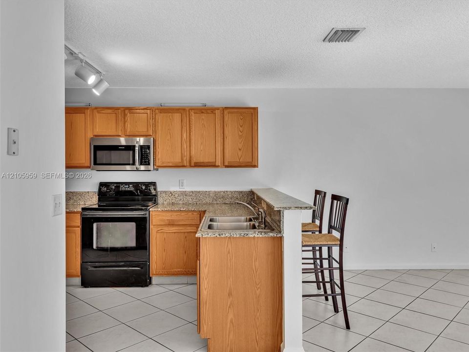Kitchen featuring wood cabinetry, stone-finish countertops, stainless steel microwave, black electric range, and tile flooring