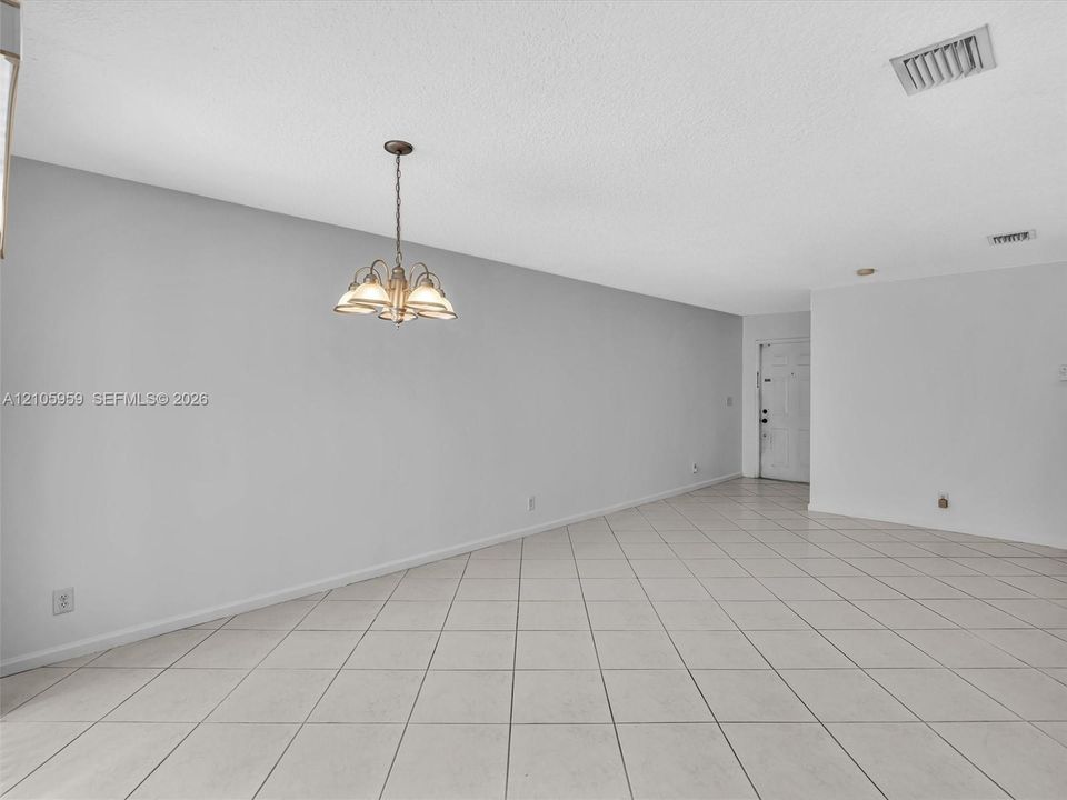 Open-concept interior featuring neutral wall tones, large-format tile flooring set on a diagonal, and a multi-arm polished metal chandelier