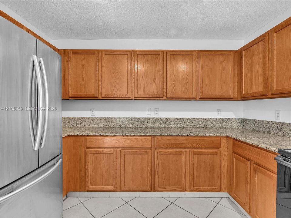 Kitchen featuring light wood-finish cabinetry, stone-patterned countertops, a matching full-height stone backsplash, and a stainless steel refrigerator