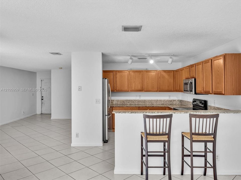 Kitchen featuring wood cabinetry, stone-surface countertops, tile flooring, stainless steel refrigerator, and integrated track lighting