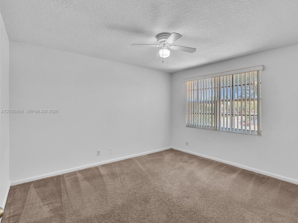Neutral-toned carpeted flooring, white wall finish, ceiling fan with integrated lighting, and vertical window blinds