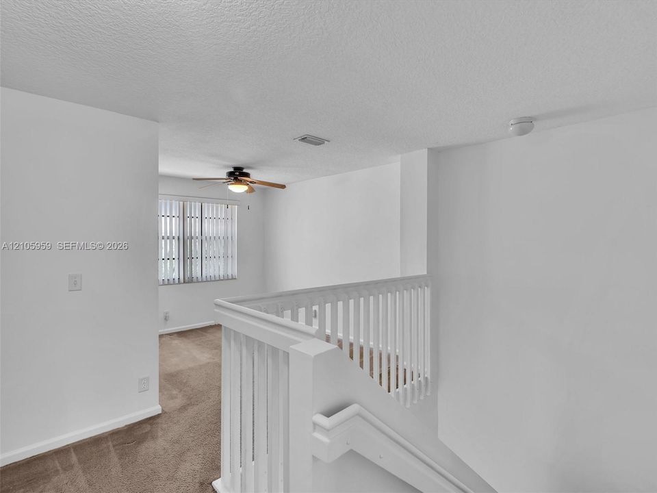 White vertical balustrade railing, wall-to-wall carpeting, ceiling fan with integrated lighting, and horizontal slatted window blinds