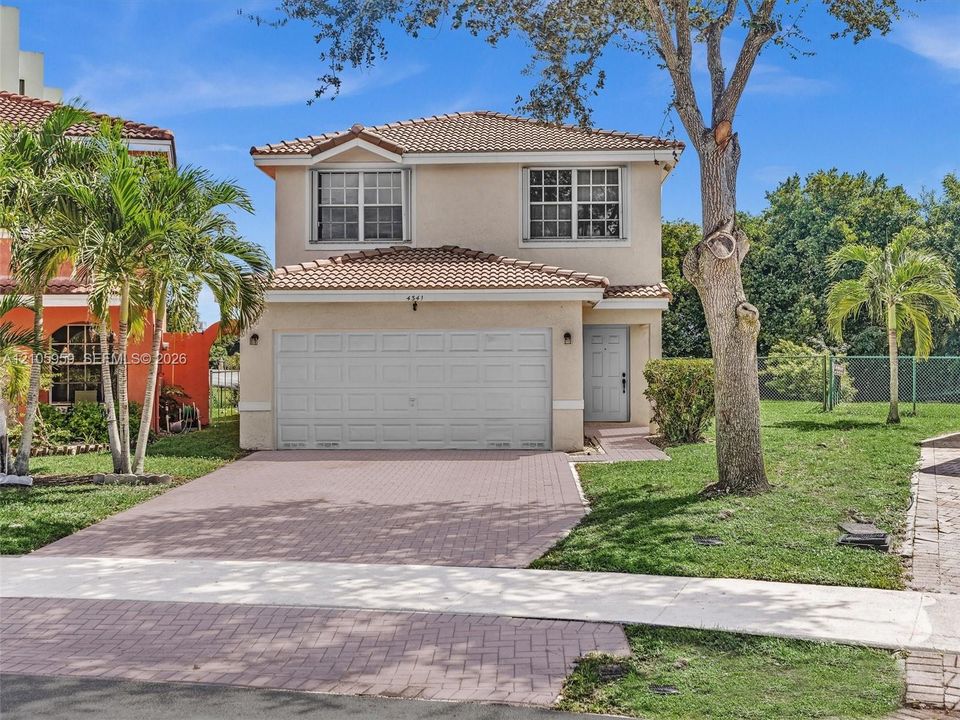 Two-story residence featuring a stucco exterior, clay tile roof, attached garage, and paved driveway