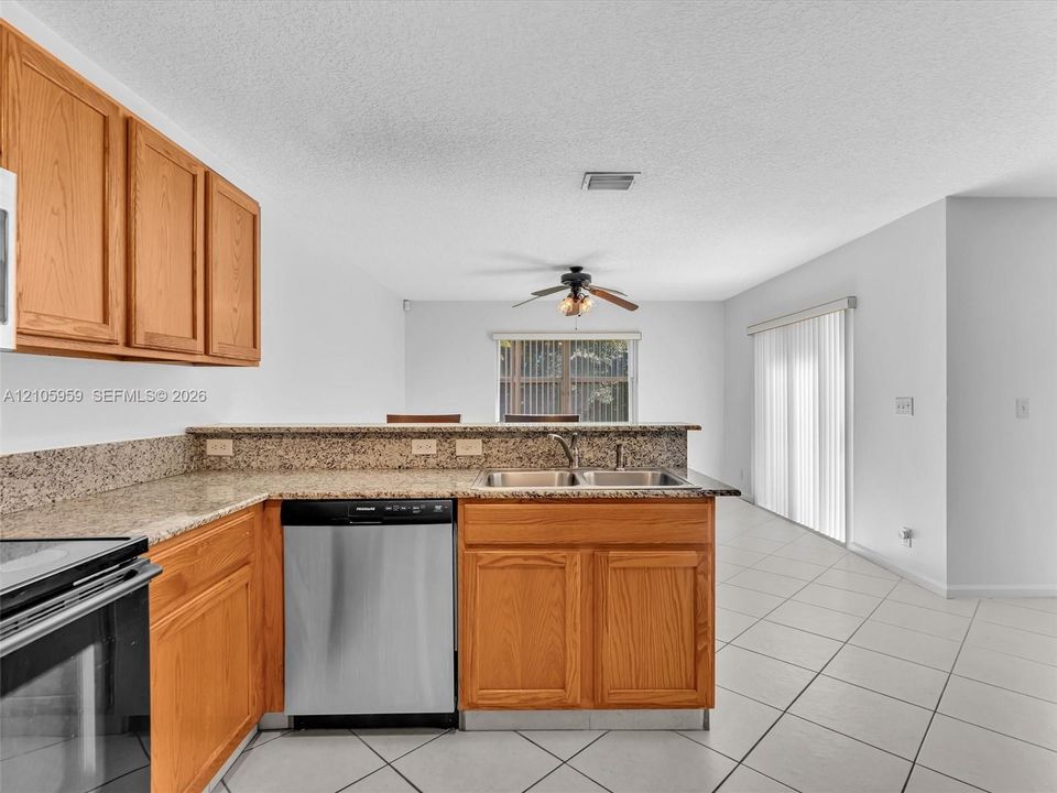 Kitchen featuring wood cabinetry, stone-finish countertops, stainless steel dishwasher, tile flooring, and sliding glass patio door