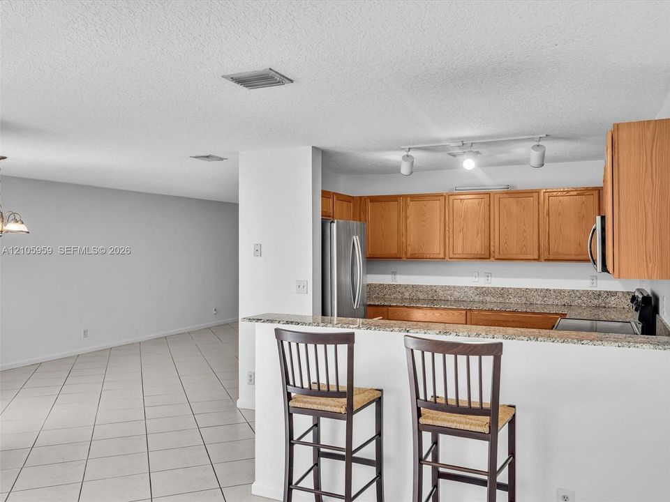 Kitchen featuring light wood cabinetry, stone-surface countertops, stainless steel appliances, and a tiled breakfast bar